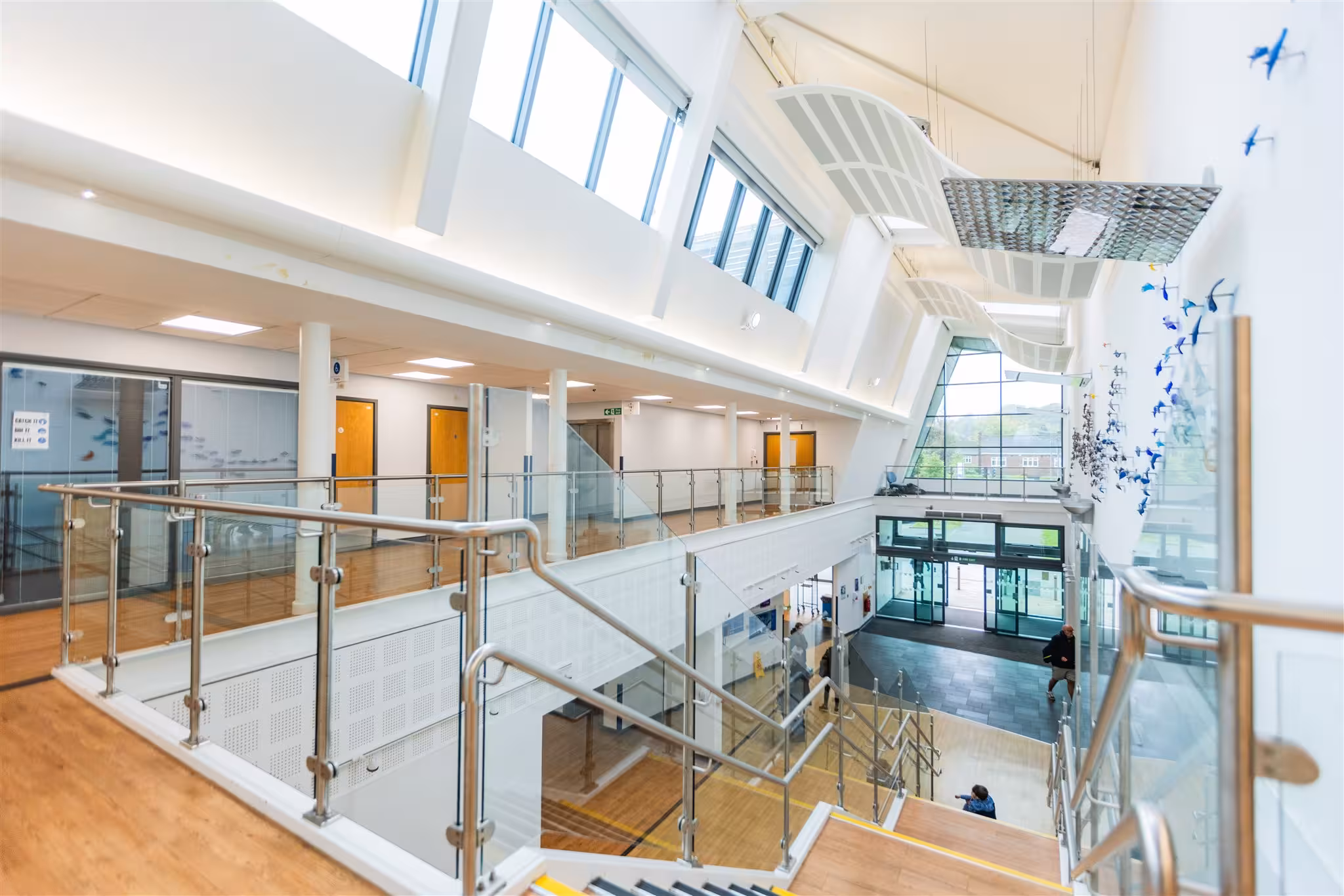 Bright, modern interior of a healthcare centre featuring a glass-panelled staircase, upper walkways, and high ceilings with skylights.