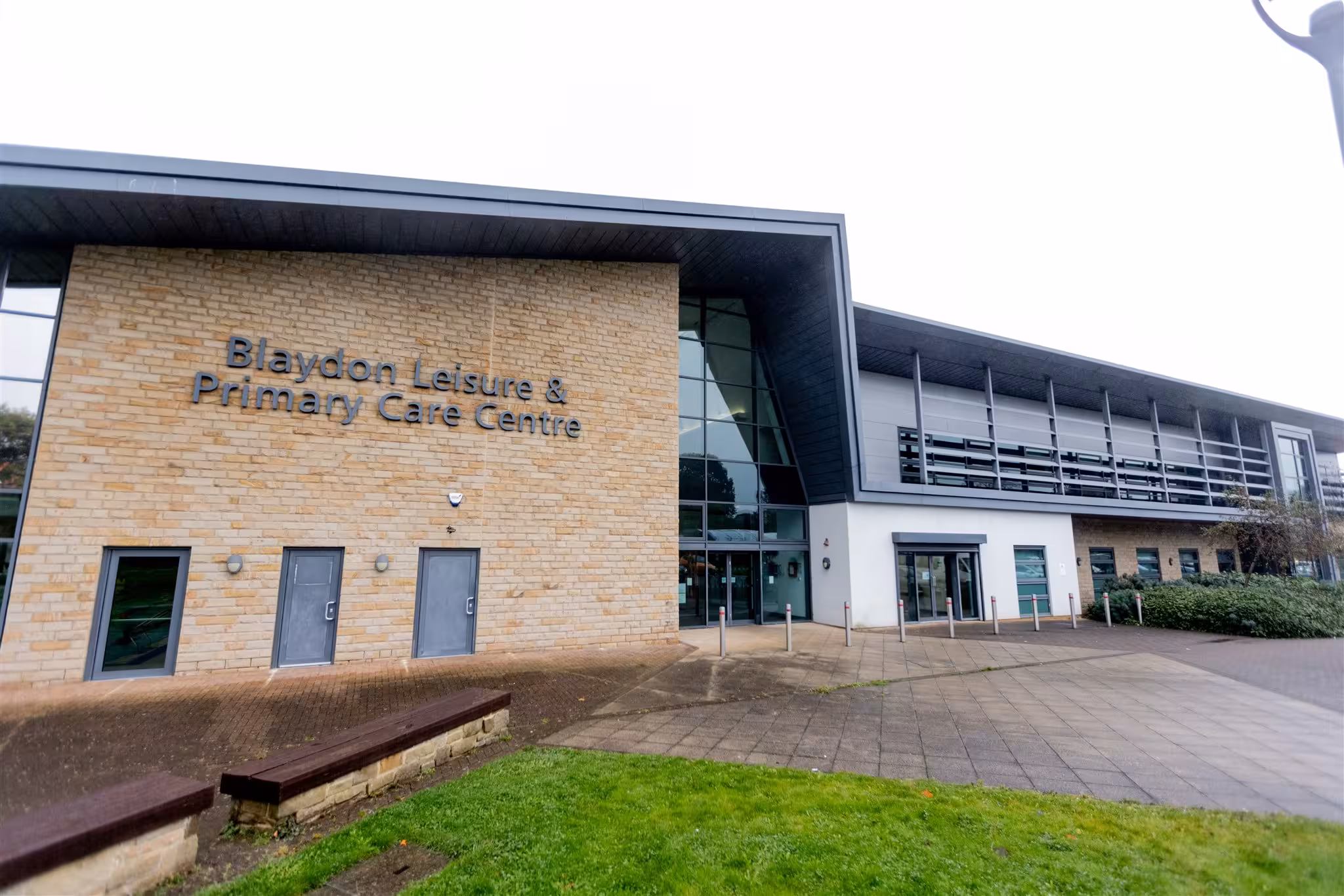 Exterior view of the Blaydon Leisure & Primary Care Centre, featuring a modern brick facade, a large glass entrance, and a paved courtyard.